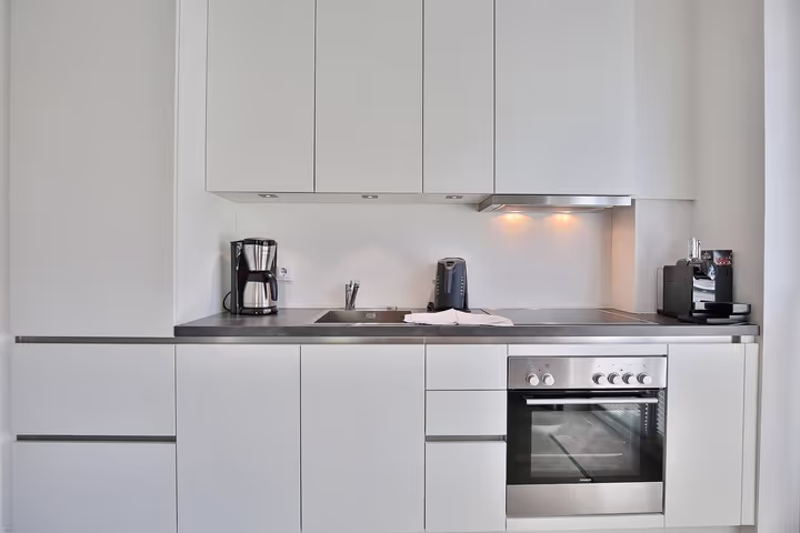 Voll ausgestattete weiße Küchenzeile mit Backofen und Kaffeemaschine